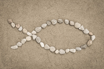 Fototapeta na wymiar Christian symbol - fish shapemade of stones on sand