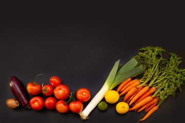 vegetables: carrots with greens, tomatoes, onions, limmons on a black background, copy space above