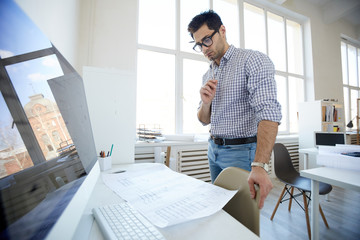 Wide angle portrait of engineer looking at plans and drafts in office, copy space