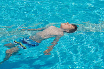 Cute European boy swimming backstroke in the pool.