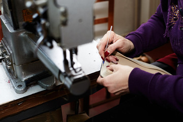 Fototapeta na wymiar A woman sews a leather strip with a special sewing machine for leather, used in the production of handbags / shoes