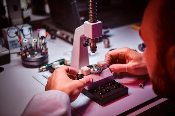 Mature watchmaker is doing engraving for custmer's watch at his workshop.