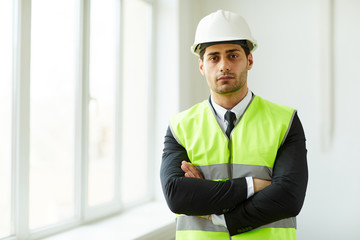 Waist up portrait of handsome engineer wearing hardhat posing on construction site and looking at camera, copy space