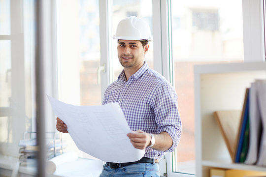 Portrait of Middle-eastern engineer holding plans posing standing by window in office, copy space