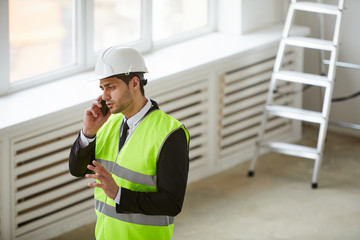 High angle portrait of Middle-Eastern engineer wearing hardhat speaking by phone while standing on construction site, copy space