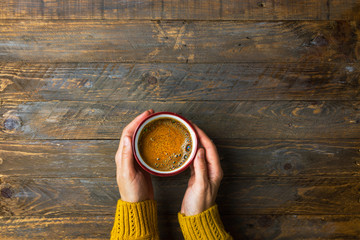 Young caucasian woman girl in knitted yellow sweater holds in hands mug with freshly brewed coffee...