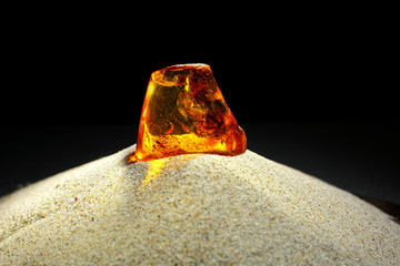 Beautiful bright amber in the sand against a black background. A piece of glowing amber with a spider. Natural mineral resin for jewelers. Sun Stone Petrified resin. Amber inclusions