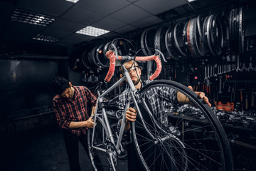 Two attractive mans are working on bicycle fixing at busy workshop.
