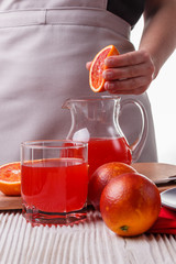 young woman in a gray apron squeezes juice of orange blood