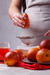 young woman in a gray apron squeezes juice of orange blood