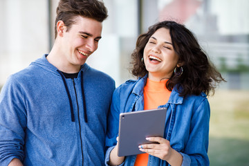 Young cute couple - a boy and a girl standing near a glass building. A couple have fun spending time together. Teens look at the tablet