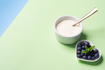Bowl of natural yogurt and fresh blueberries in heart shaped plate on pastel green background. Healthy breakfast concept