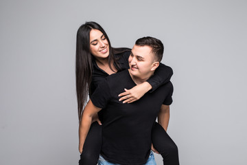 Young fun couple having fun riding piggy back laughing on grey background