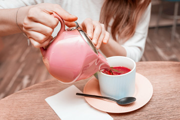 The girl pours from the kettle into a mug of fragrant fruit red tea