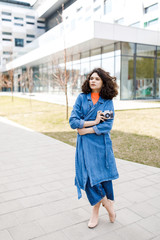 Young pretty girl walking on the street, dressed in jeans and denim shirt. Student weekdays. Cute girl holds the camera of the old model