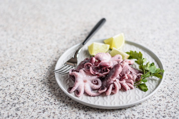 Baby octopus in a gray plate with lime and herbs on gray background. Selective focus
