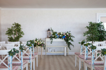 View of a wedding ceremony scene in a room with several rows of white chairs and compositions from different flowers