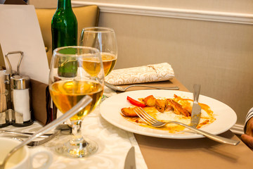 Half eaten meal and two glasses of beer on the table in restaurant. Leftover of fried potatoes and meat on white plate