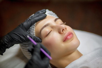 Permanent make up eyeliner procedure, applying on young girl. Close-up. Young beautiful woman...