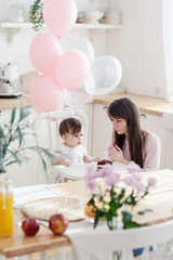 Obraz na płótnie Canvas Loving young mother teaching her baby daughter how to blow out candle on her first birthday cake and make a wish