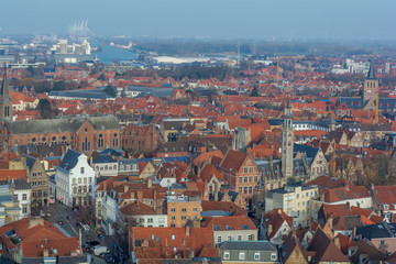 Fototapeta na wymiar Fantastic Bruges city skyline with red tiled roofs, The Poortersloge (Burgher’s Lodge) tower and windmills in the background. View to Bruges medieval cityscape from the top of the Belfry Tower.