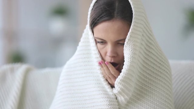 Covered with plaid young woman freezing feeling cold at home