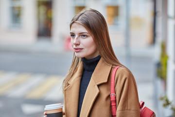 Young stylish woman drinking coffee to go in a city street 