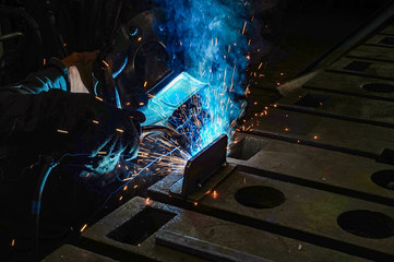 The working welder performs welding work in production using electric arc metal welding.