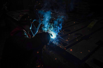 The working welder performs welding work in production using electric arc metal welding.