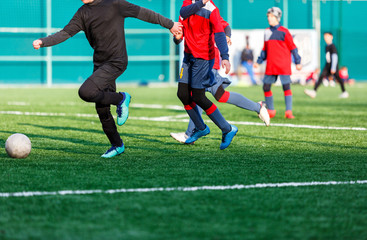 Boys at black red sportswear run, dribble, attack on football field. Young soccer players with ball on green grass. Training, football, active lifestyle for kids  