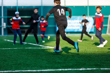 Boys at black red sportswear run, dribble, attack on football field. Young soccer players with ball on green grass. Training, football, active lifestyle for kids  