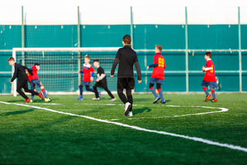 Boys at black red sportswear run, dribble, attack on football field. Young soccer players with ball on green grass. Training, football, active lifestyle for kids  