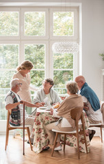 Elderly friends spending time together by drinking tea and enjoying photos in common dining room of...