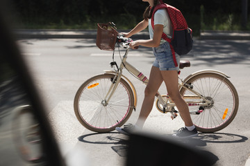 Schoolgirl with backpack and bike crossing street in front of a car