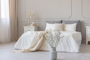 White flowers in vase in elegant grey bedroom interior with simple bedding