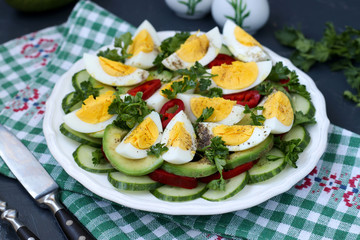 Useful salad of avocado, cucumbers, eggs and sweet pepper located in a plate against a dark background