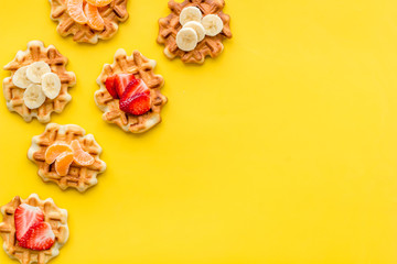 Breakfast with Belgian waffles with strawberry, tangerine and banana topings on yellow background top view mock up