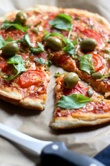 Homemade vegetarian pizza with tomato sauce, two types of cheese, tomatoes, peppers, arugula, olives and herbs. Selective focus.