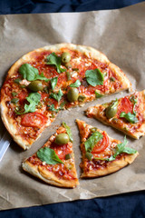 Homemade vegetarian pizza with tomato sauce, two types of cheese, tomatoes, peppers, arugula, olives and herbs. Selective focus.