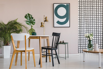 Modern poster on pastel pink wall of elegant living room interior with round wooden table with chairs