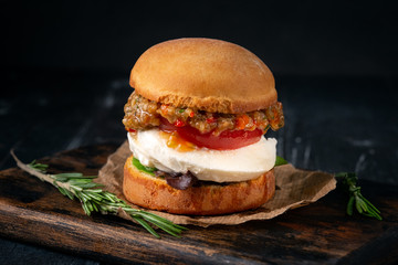 Vegetarian Burger made from fried eggplant, tomato, lettuce, avocado and mozzarella cheese on a wooden Board and dark background