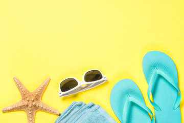 Blue flip flops, swimsuit, sunglasses and starfish on yellow background.
