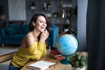 Smiling beautiful woman with a model of the globe indoor.