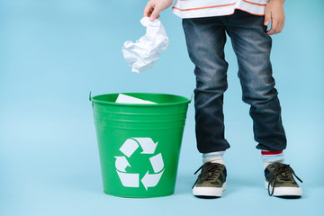 Child is throwing crumpled paper in recycling bin.