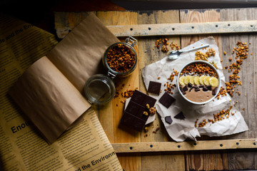 asty breakfast from chocolate smoothie bowl topping with banana, homemade granola and chocolate pieces with coconut milk served on the wood table early in the morning