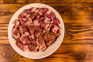 Ceramic plate with raw chicken hearts on wooden table. Top view