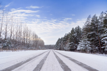 Fototapeta premium Patterns on the winter highway in the form of four straight lines. Snowy road on the background of snow-covered forest. Winter landscape.