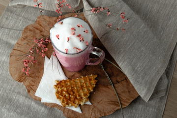 pink coffee latte macchiato with foamy flowers decorated with sweet waffles baking