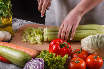 young woman in a gray apron cuts a celery
