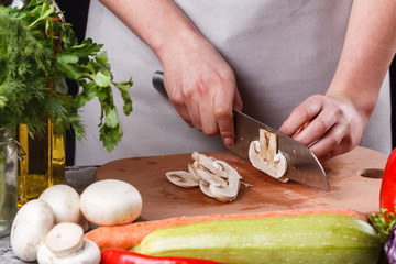 young woman slicing mushrooms in a gray apron